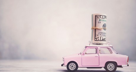 A toy pink car has cash on top. [Factors that Affect Car Insurance Rates]